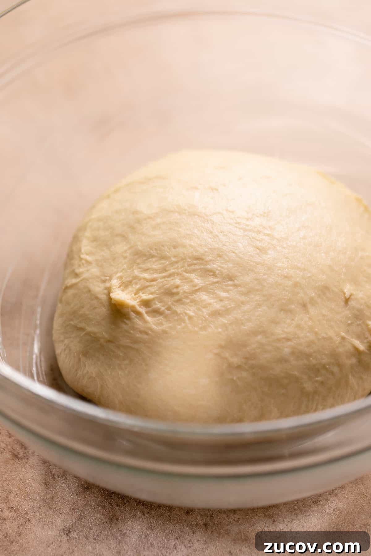 A smooth donut dough ball in a glass bowl.