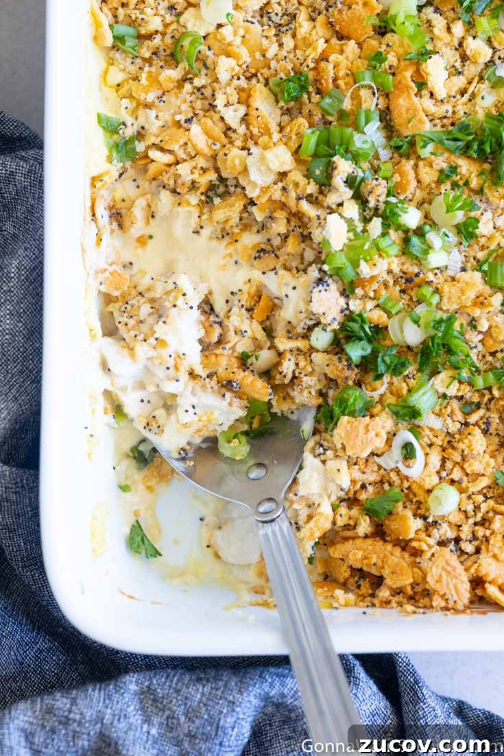 This poppy seed chicken is a classic, super creamy chicken casserole your family will love. You're going to want to put this one into your regular dinner rotation! #chickencasserole #poppyseedchicken A portion taken out poppy seed chicken with ritz crackers in a casserole
