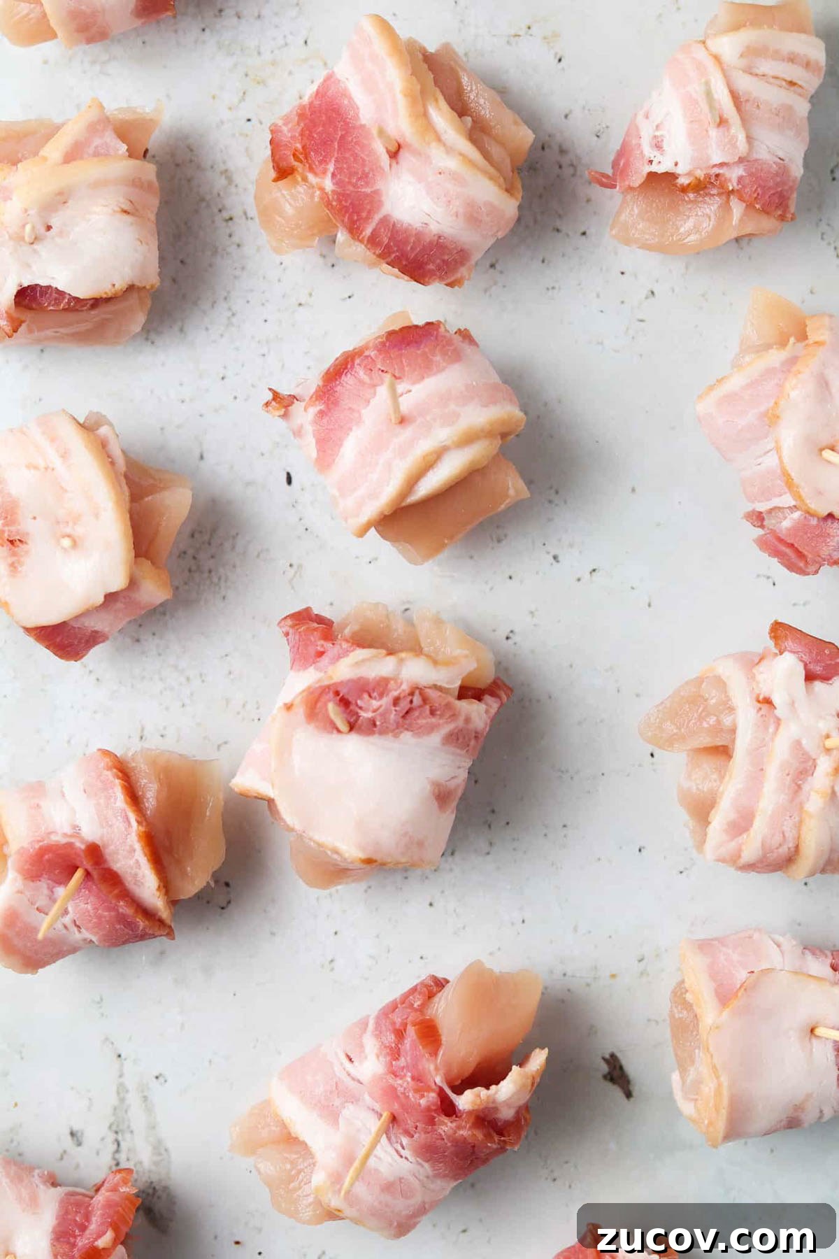 Crispy Bacon-Wrapped Chicken Bites with Maple Glaze 4 Raw bacon wrapped chicken bites with tooth picks on a tray.