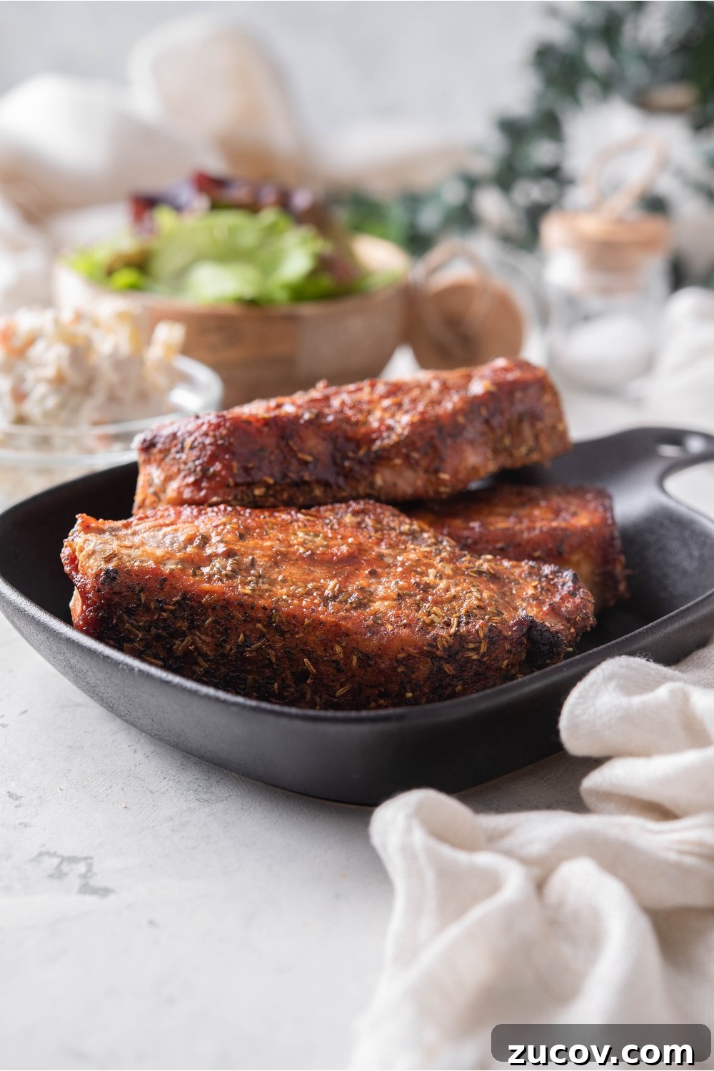 Oven-Baked Boneless Country-Style Pork Ribs — Juicy and Tender 3 A stack of three seasoned barbecue pork ribs on a black plate.
