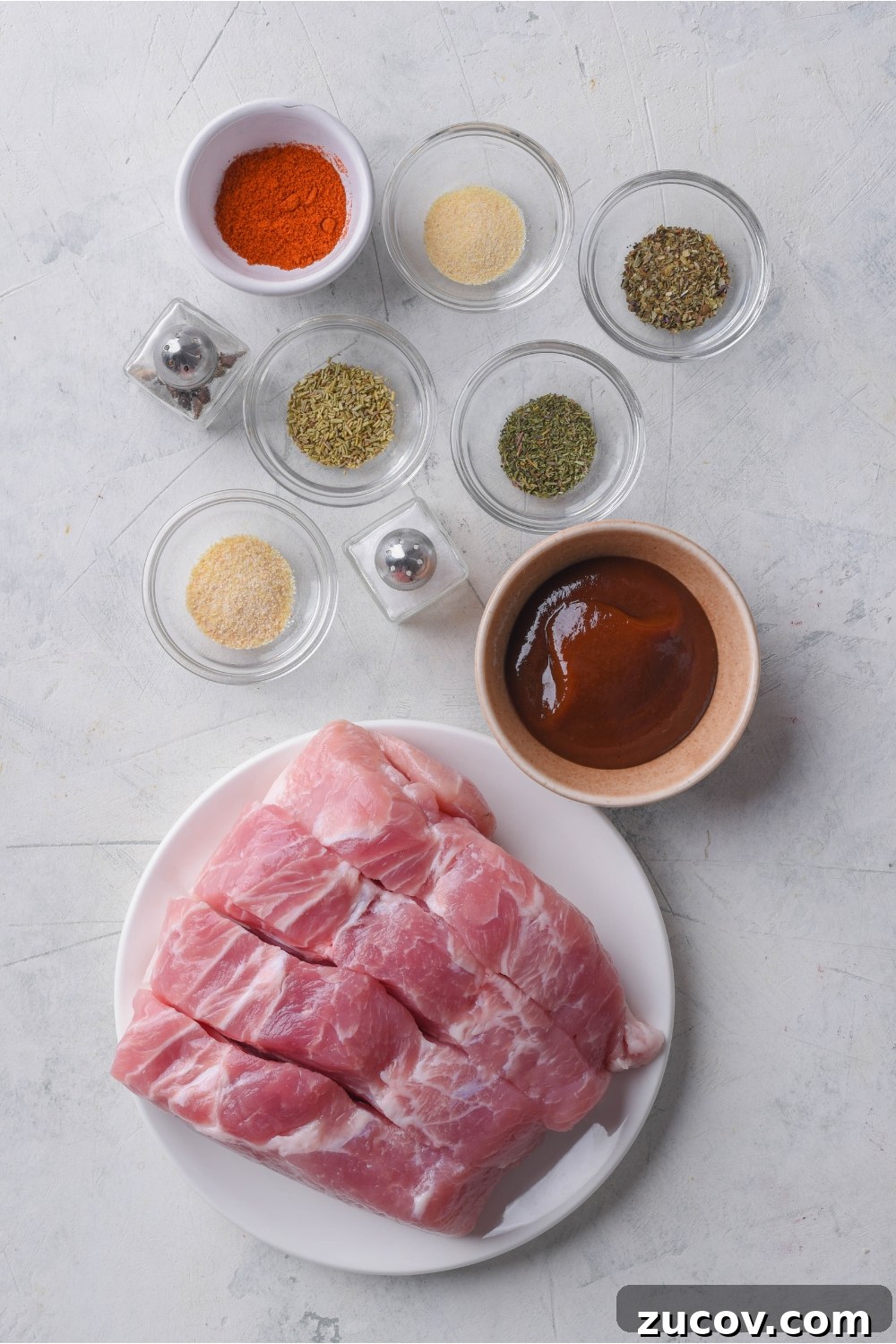 Oven-Baked Boneless Country-Style Pork Ribs — Juicy and Tender 4 Overhead view of an assortment of ingredients including a plate of boneless pork ribs and bowls of barbecue sauce, various seasonings, and mini salt and pepper shakers.