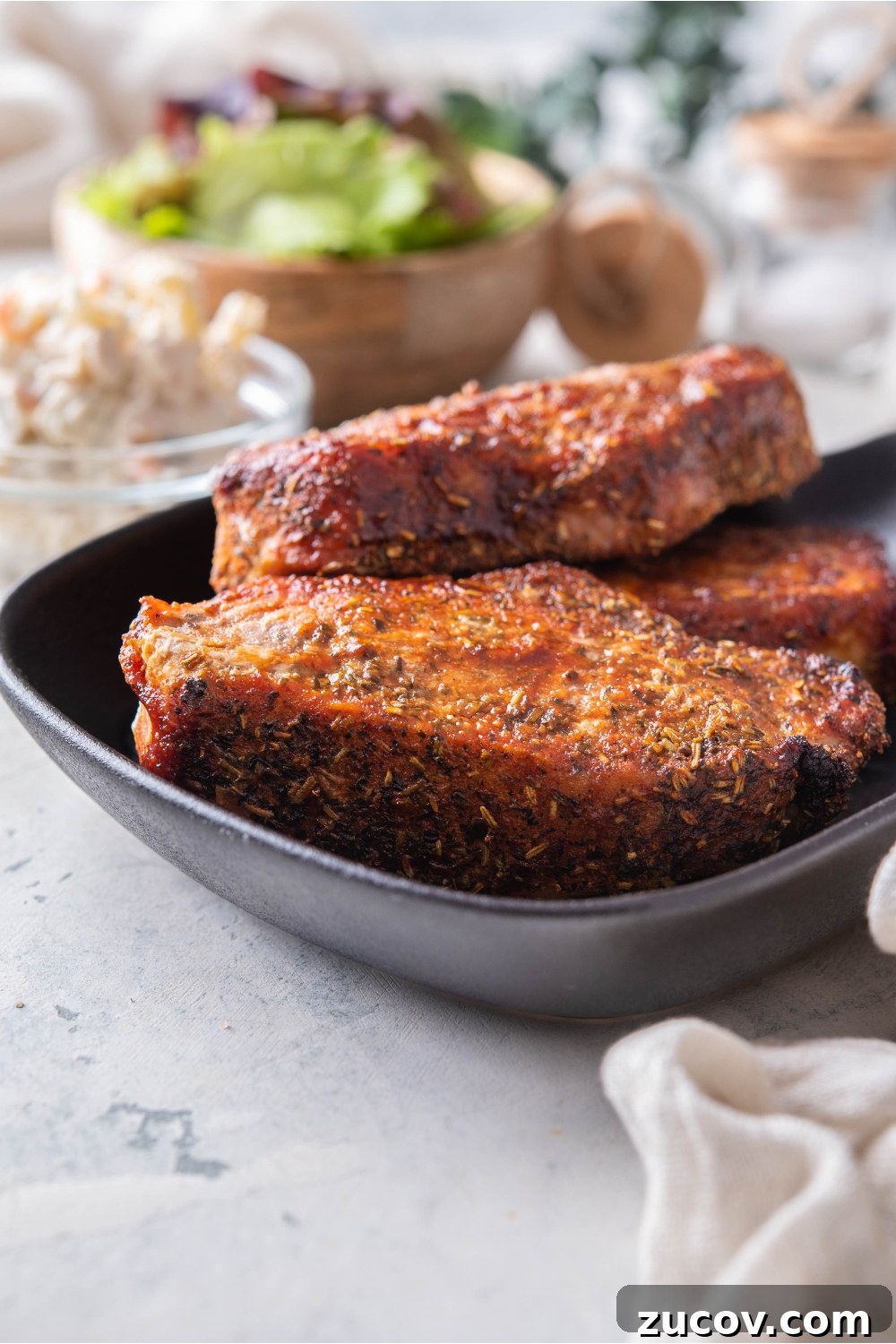 Oven-Baked Boneless Country-Style Pork Ribs — Juicy and Tender 9 A stack of three seasoned barbecue pork ribs on a black plate.