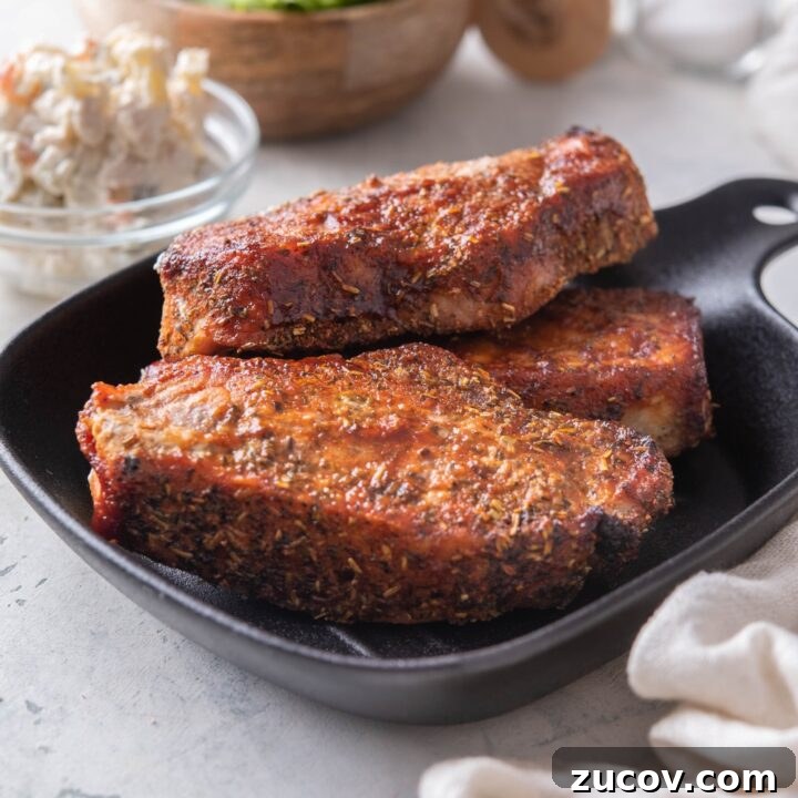 A stack of three seasoned barbecue pork ribs on a black plate.
