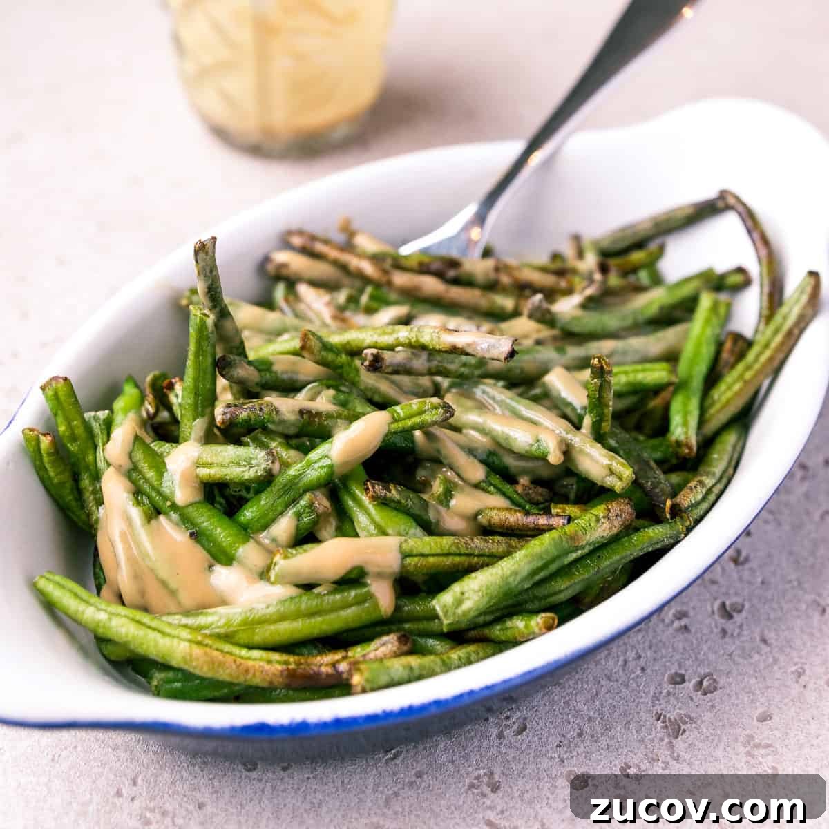 Photo of a dish of air fried green beans mixed with tahini and tamari sauce.