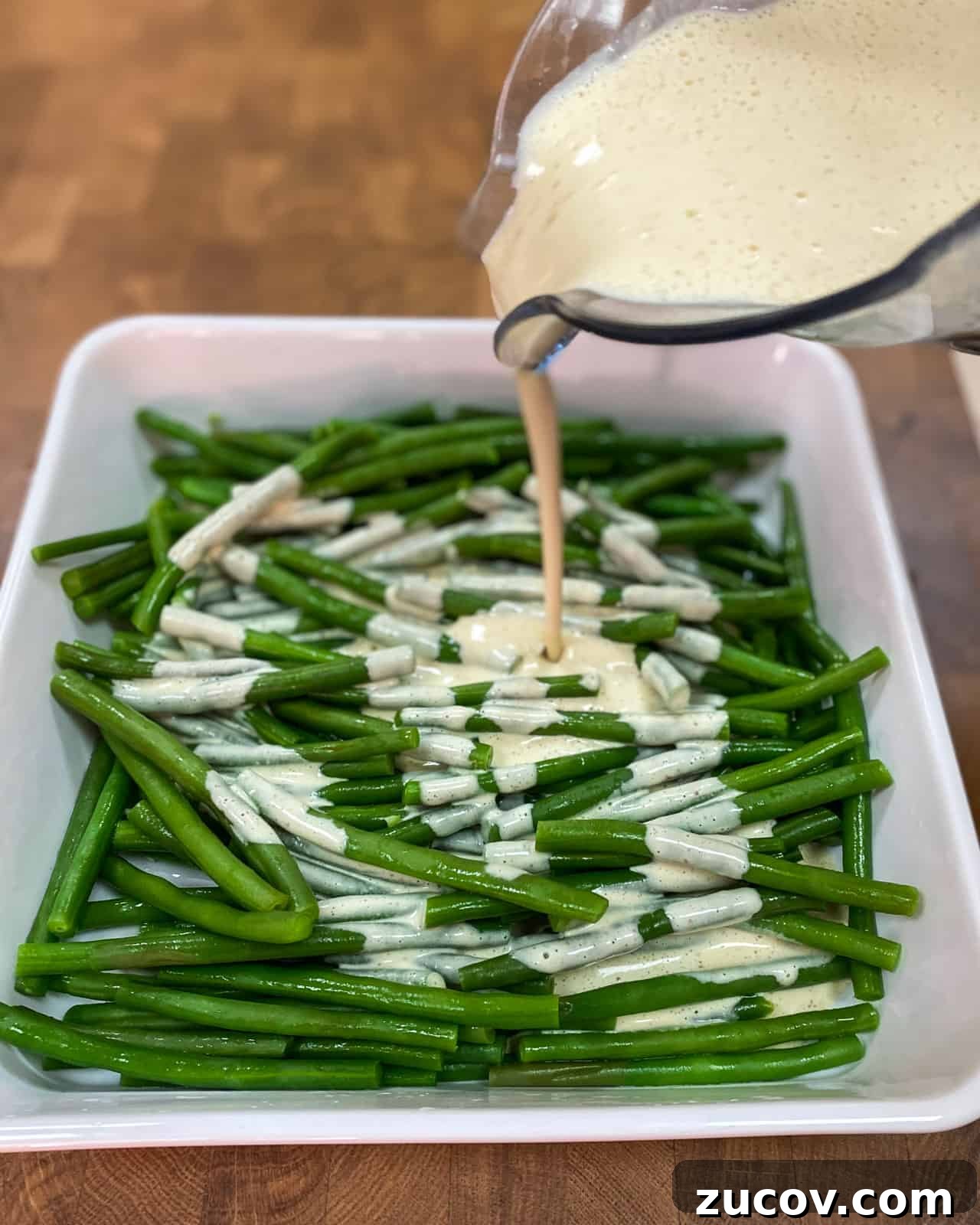Vegan Green Bean Casserole Recipe with Crispy Onion Topping 7 Photo of cashew sauce being poured over the cooked green beans.
