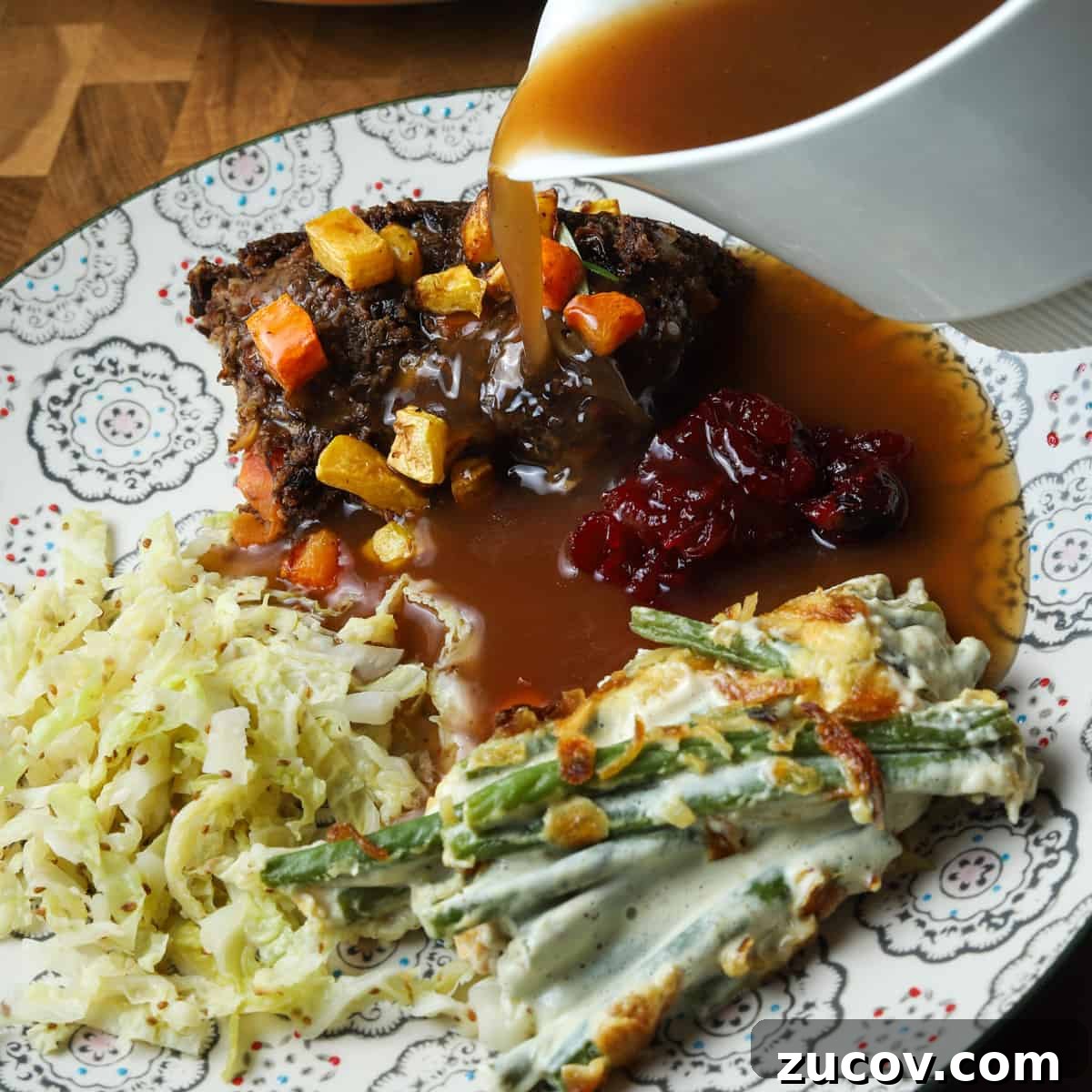 Vegan Green Bean Casserole Recipe with Crispy Onion Topping 9 Photo of a plate with nut roast, cabbage, green bean casserole, cranberry sauce and gravy being poured over the top.