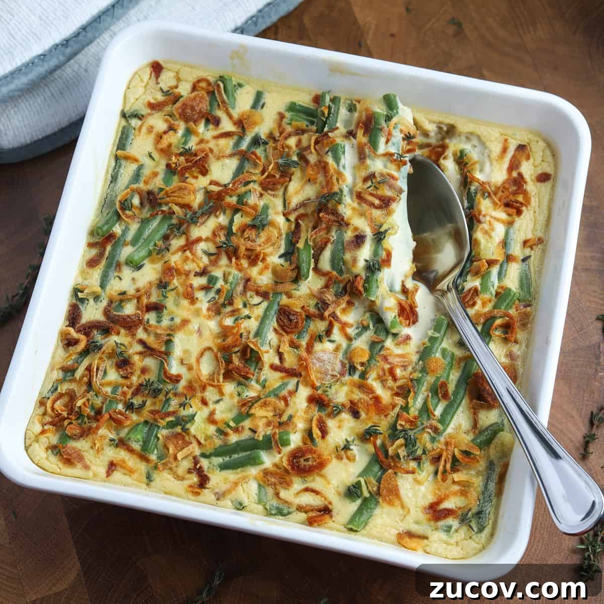 Vegan Green Bean Casserole Recipe with Crispy Onion Topping 10 Overhead photo of a square white ceramic dish filled with freshly baked vegan green bean casserole and a serving spoon ready to serve.
