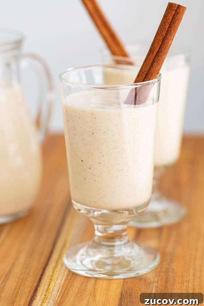 Classic Eggnog Recipe: Spiked and Alcohol-Free Versions 2 glass of eggnog with a cinnamon stick on a wooden surface