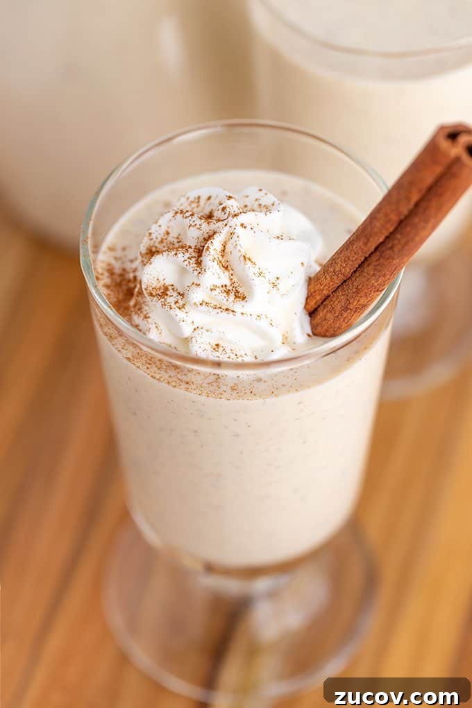 Classic Eggnog Recipe: Spiked and Alcohol-Free Versions 6 picture showing the cinnamon dusted whipped cream on top of the eggnog on a wood surface