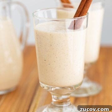 Classic Eggnog Recipe: Spiked and Alcohol-Free Versions 7 glass of eggnog with a cinnamon stick on a wooden surface