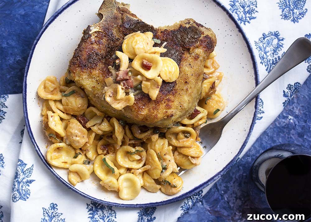 Cheese stuffed pork chops with pasta. Top view of a plate with a breaded pork chop and orecchiette tossed in a creamy sauce.