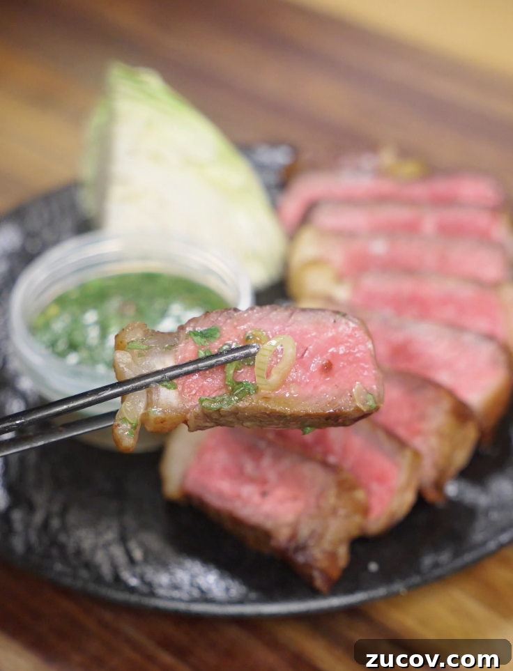 Crying Tiger Steak Recipe: Grilled Thai Marinated Flank Steak 3 Close-up of a chopsticks bite of medium-rare Crying Tiger Steak dipped in Thai-style sauce, showing juicy steak and fresh herbs.