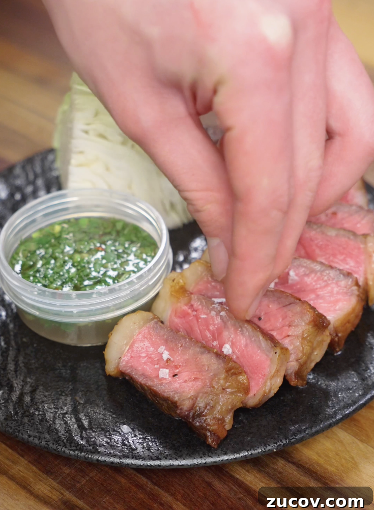 Crying Tiger Steak Recipe: Grilled Thai Marinated Flank Steak 8 Flaky salt being sprinkled over sliced Crying Tiger Steak just before serving to enhance flavor and texture.