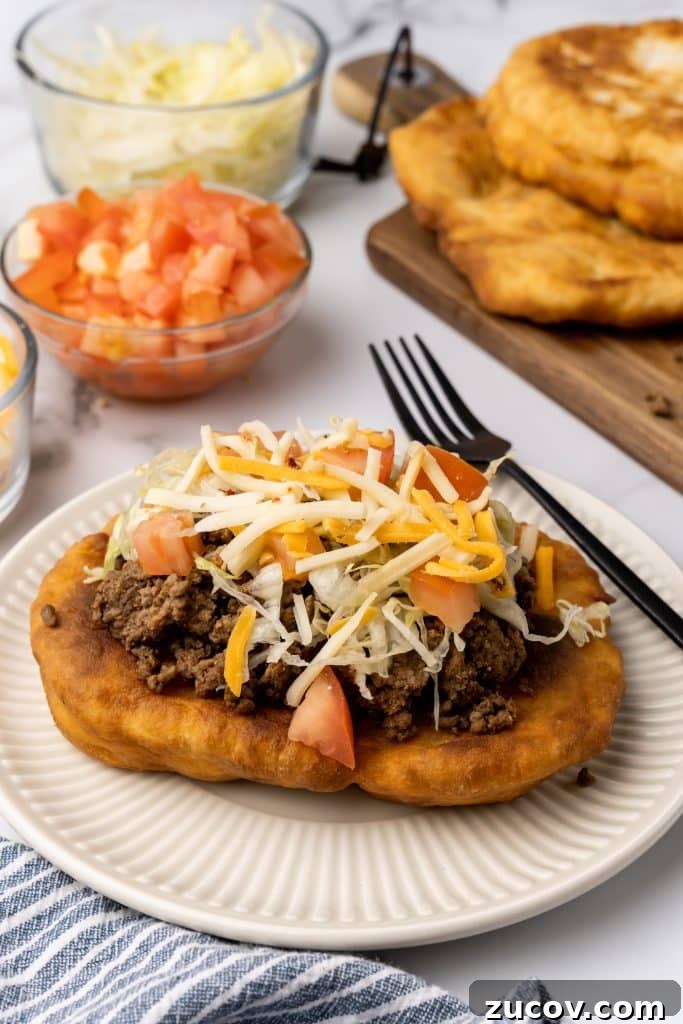 Navajo Tacos: Authentic Indian Fry Bread Recipe & Tips 12 loaded navajo fry bread taco on a white plate next to a black fork
