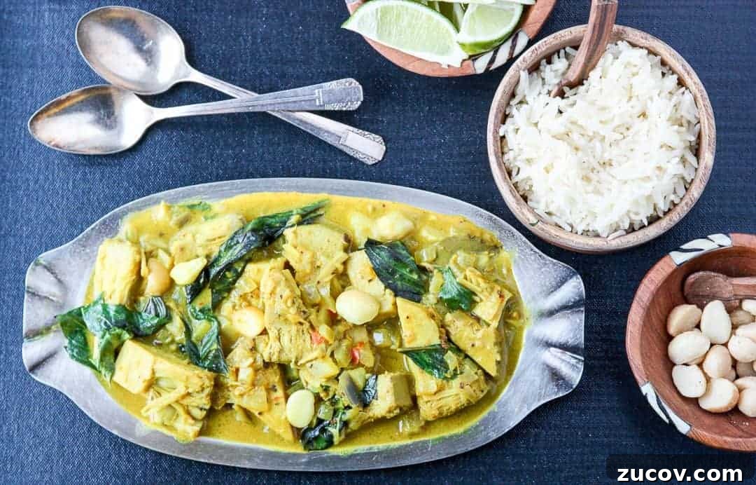 A plate of vegetarian curry on a table, with dishes of rice and lime wedges