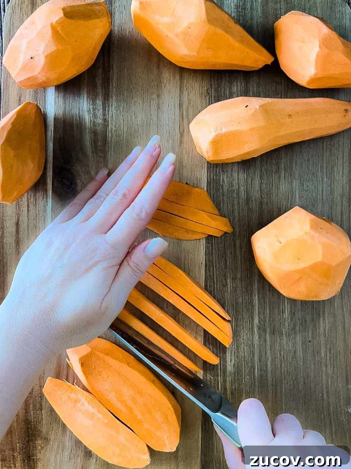 Crispy Air-Fryer Sweet Potato Fries Coated in Cornstarch 5 A hand using a sharp knife to cut the sweet potatoes into fries.