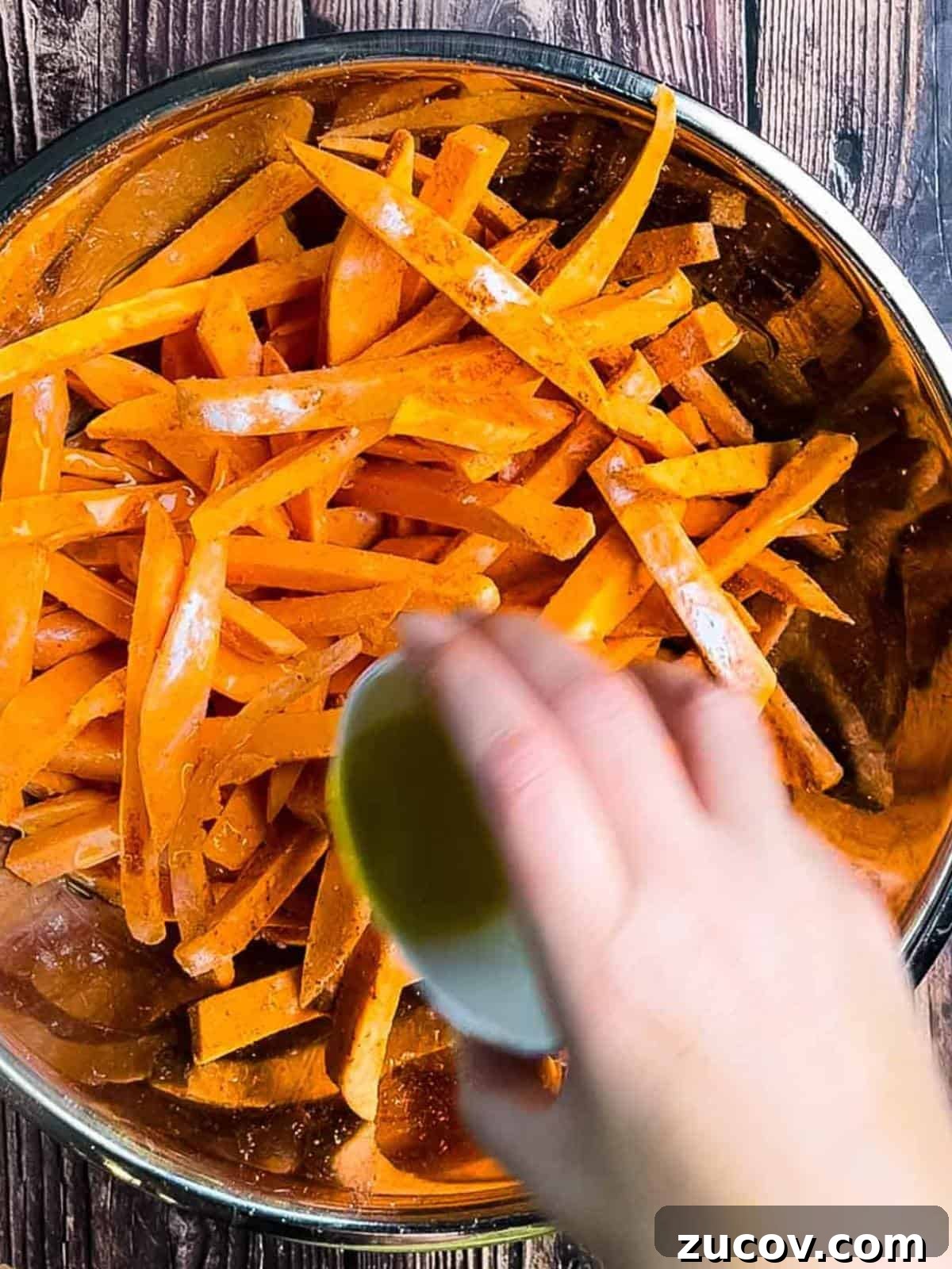 Crispy Air-Fryer Sweet Potato Fries Coated in Cornstarch 10 A hand drizzling oil onto the fries in the large bowl.
