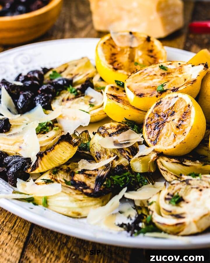 Grilled Fennel Salad - sipandfeast.com #grilledfennel #fennel #italiansalad #salad Fennel salad in plate with a block of parmesan, a vegetable peeler and a bowl of olives in background.