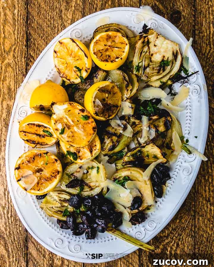 Grilled Fennel Salad - sipandfeast.com #grilledfennel #fennel #italiansalad #salad Grilled fennel and lemons with black olives and shaved cheese on white plate on wood table.