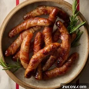 Savory Sausage-Wrapped Puff Pastry Bites for Parties 8 A close up of a dish of Pigs in Blankets decorated with sprigs of rosemary.