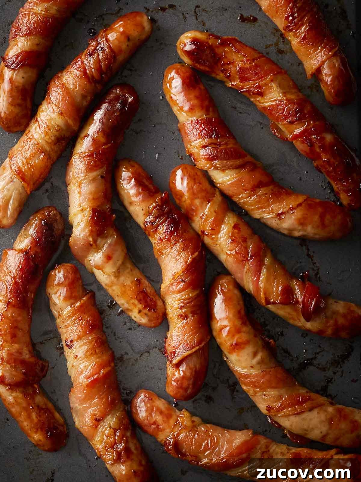 Savory Sausage-Wrapped Puff Pastry Bites for Parties 3 Pigs in Blankets on a black oven tray.