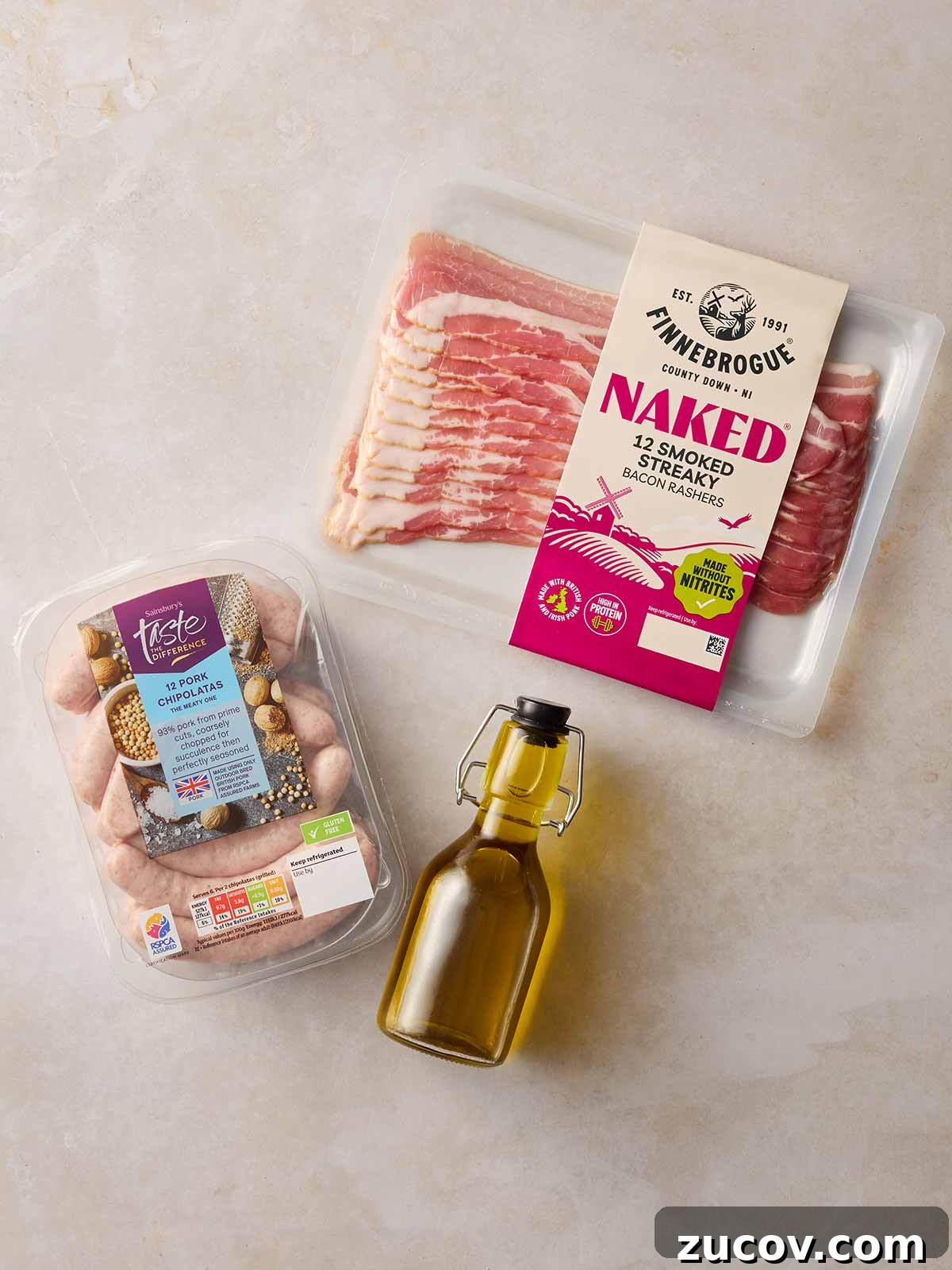 Savory Sausage-Wrapped Puff Pastry Bites for Parties 5 The ingredients for everything you need for making Pigs in Blankets at home laid out on a white surface, including bacon, sausages and oil.