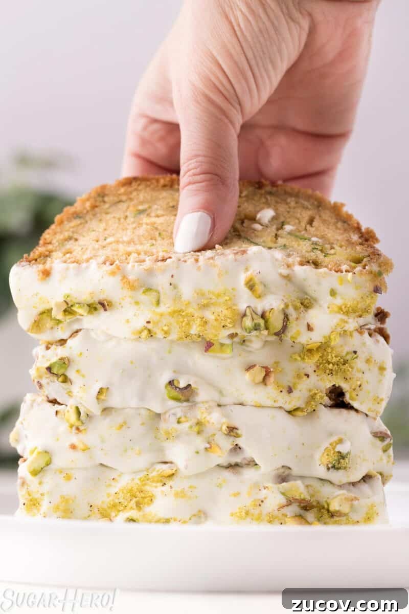 Moist Zucchini Bread Recipe with Cinnamon and Walnuts 2 A stack of zucchini bread frosted with cream cheese frosting, with a hand lifting up the top piece of bread.