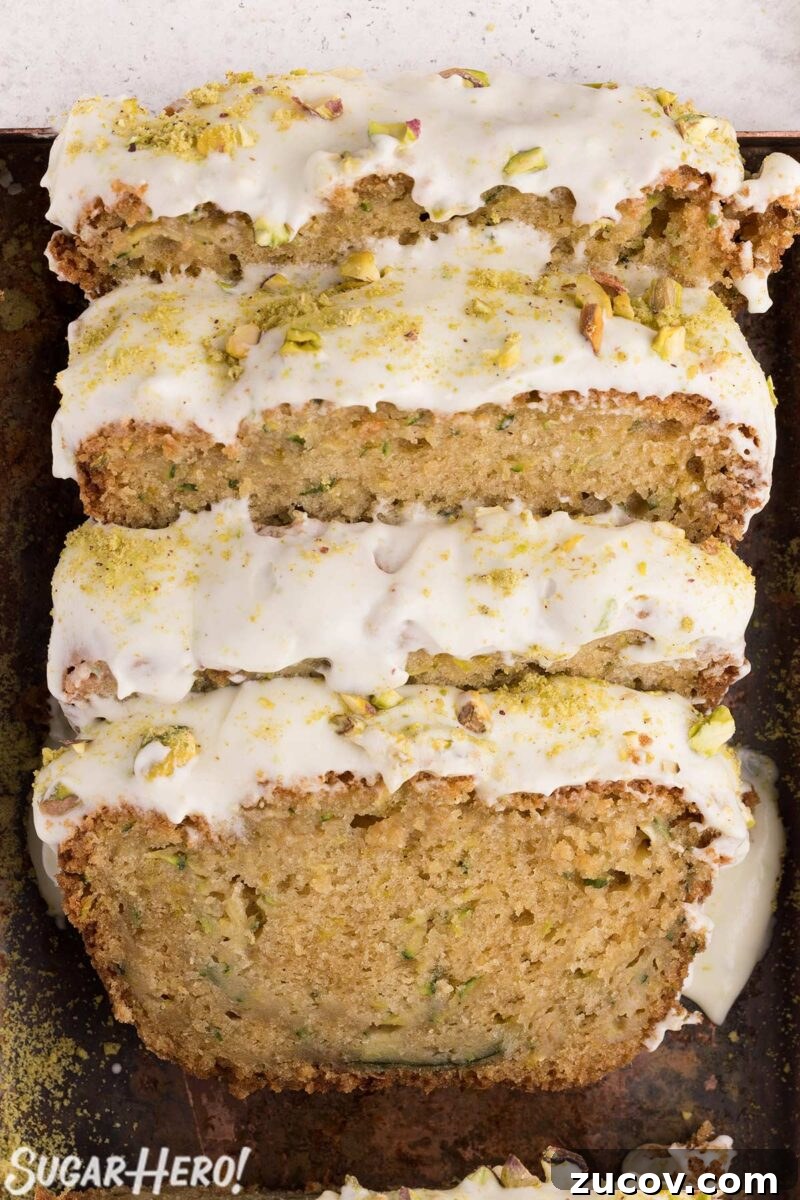 Moist Zucchini Bread Recipe with Cinnamon and Walnuts 12 Slices of zucchini bread, with cream cheese frosting on top, resting against each other in a bread pan.