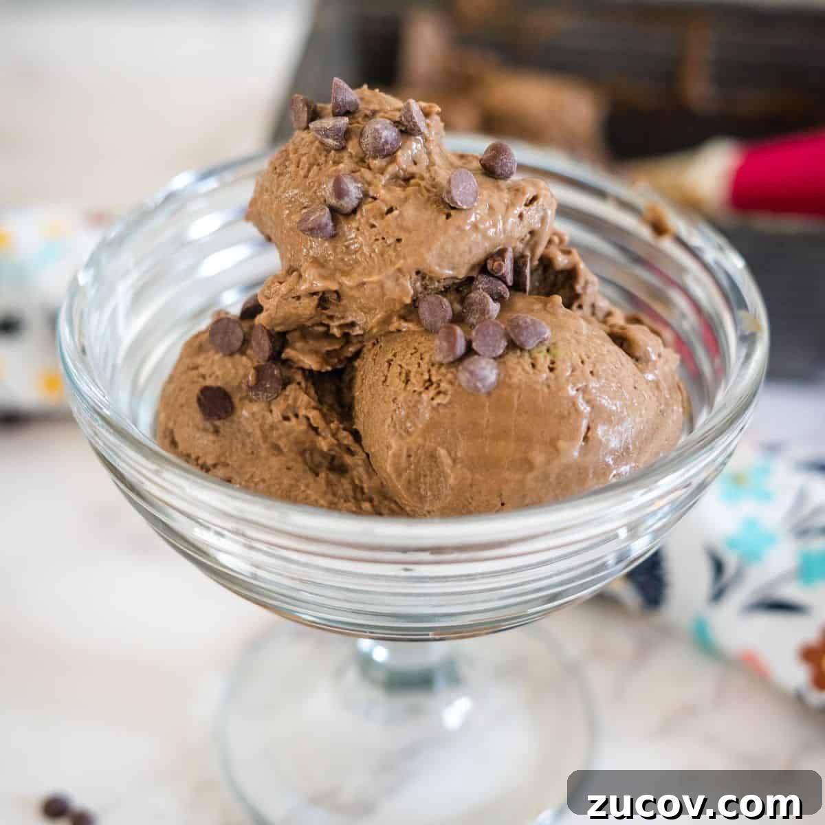 Keto Peach Ice Cream Recipe: Creamy Low-Carb Frozen Dessert 6 A glass dessert bowl filled with several scoops of chocolate ice cream topped with chocolate chips.