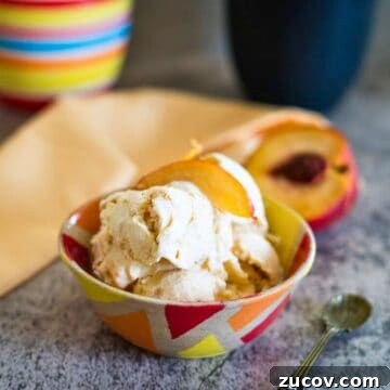 Keto Peach Ice Cream Recipe: Creamy Low-Carb Frozen Dessert 10 A bowl of ice cream topped with peach slices sits on a table, with a spoon beside it and a colorful cup and napkin in the background.