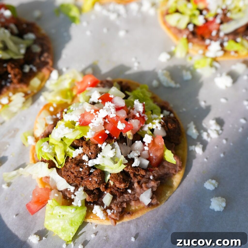 Crispy Ground Beef Tostadas with Fresh Salsa and Cheese 3 Ground beef tostadas topped with refried beans, lettuce, tomatoes, onions and queso fresco.