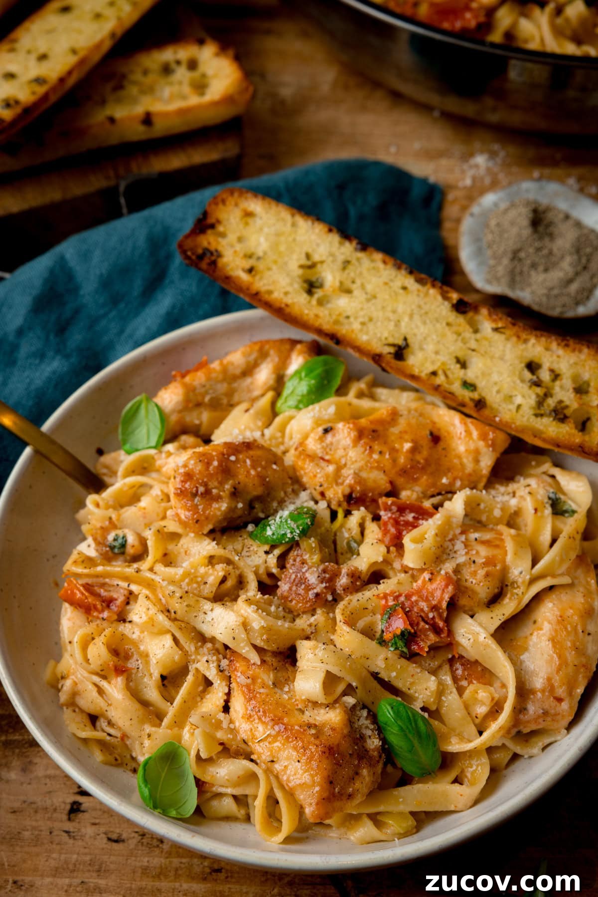 Creamy Marry Me Chicken Pasta Recipe for Weeknight Dinners 5 A tall shot of Marry Me Chicken Pasta in a white bowl with a gold fork and garlic bread.