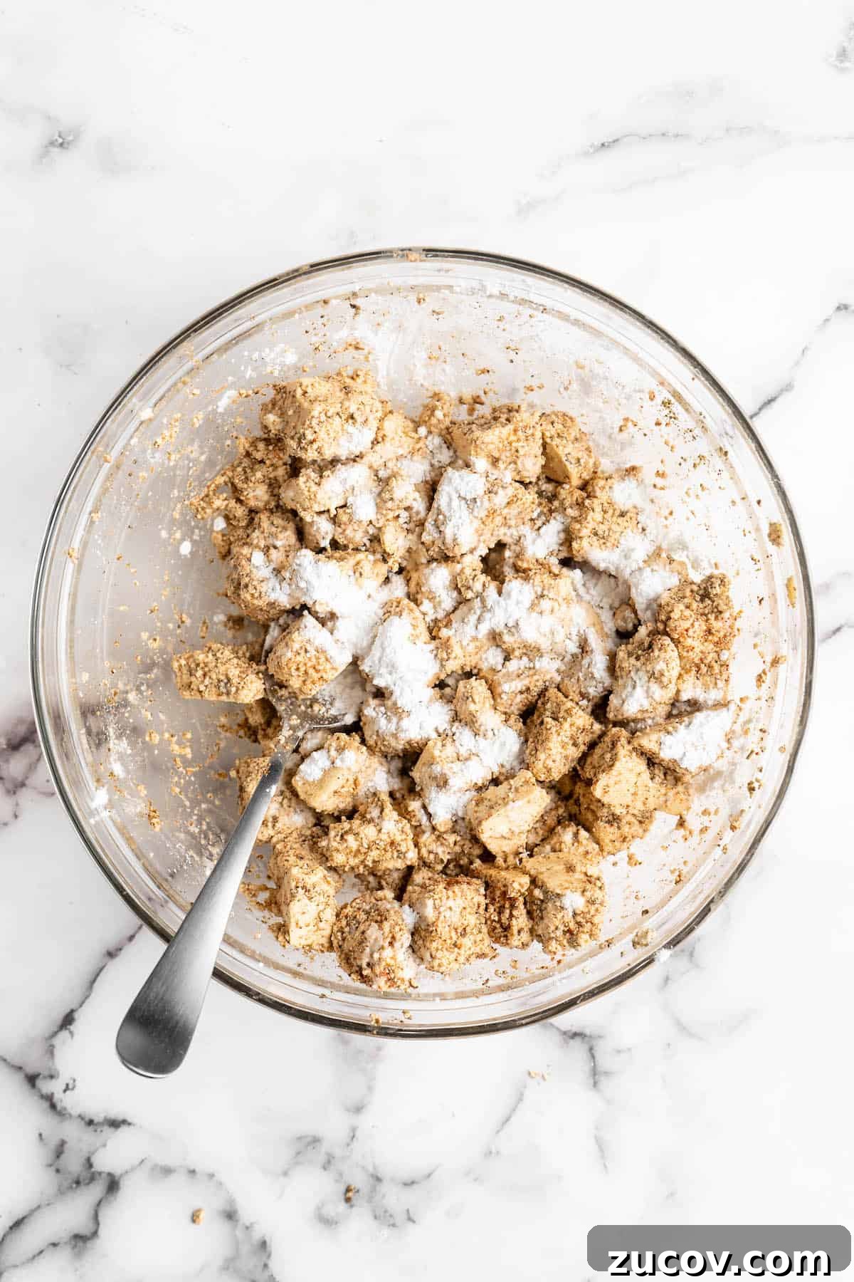 This Jamaican jerk tofu is the real deal! It's spicy, saucy, and just a little bit sweet. It's also super easy to make for a weeknight meal! Overhead view of tofu tossed with cornstarch in glass bowl