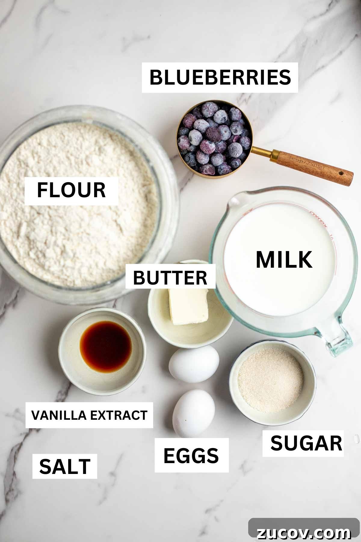 Blueberry Dutch Baby Pancake Recipe for Brunch and Dessert 3 Jars and bowls of flour, milk, sugar, eggs, butter, vanilla extract, etc on a countertop.