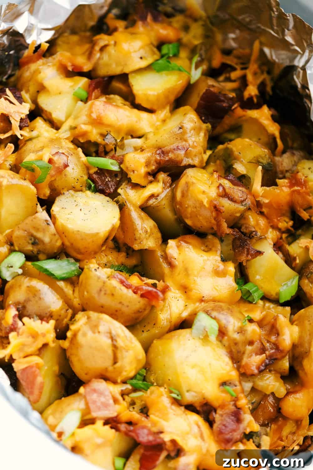 Perfectly tender and packed with flavor. All of the flavors combined with cheese and bacon to create these perfectly tender and delicious potatoes. Up close photo of the cheesy ranch bacon potatoes in a slow cooker with foil.