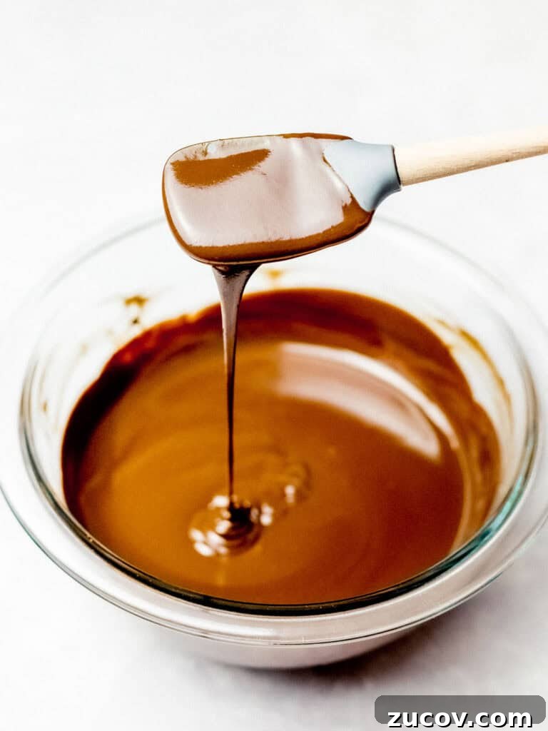 5-Minute Chocolate Ganache Recipe for Cakes, Glazes & Dips 2 chocolate ganache dripping off a spatula into a glass bowl