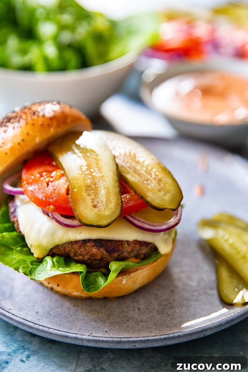 Juicy Homemade Burger Recipe for Perfect Grilling 3 a burger topped with cheese, sliced onion, tomato and pickles resting on the bottom half of a bun