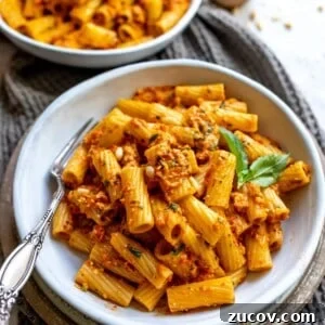 Roasted Red Pepper Pesto Recipe for Pasta, Sandwiches & Dips 11 White bowl with pesto and red peppers and noodles. A black fork in the bowl with grey towel.