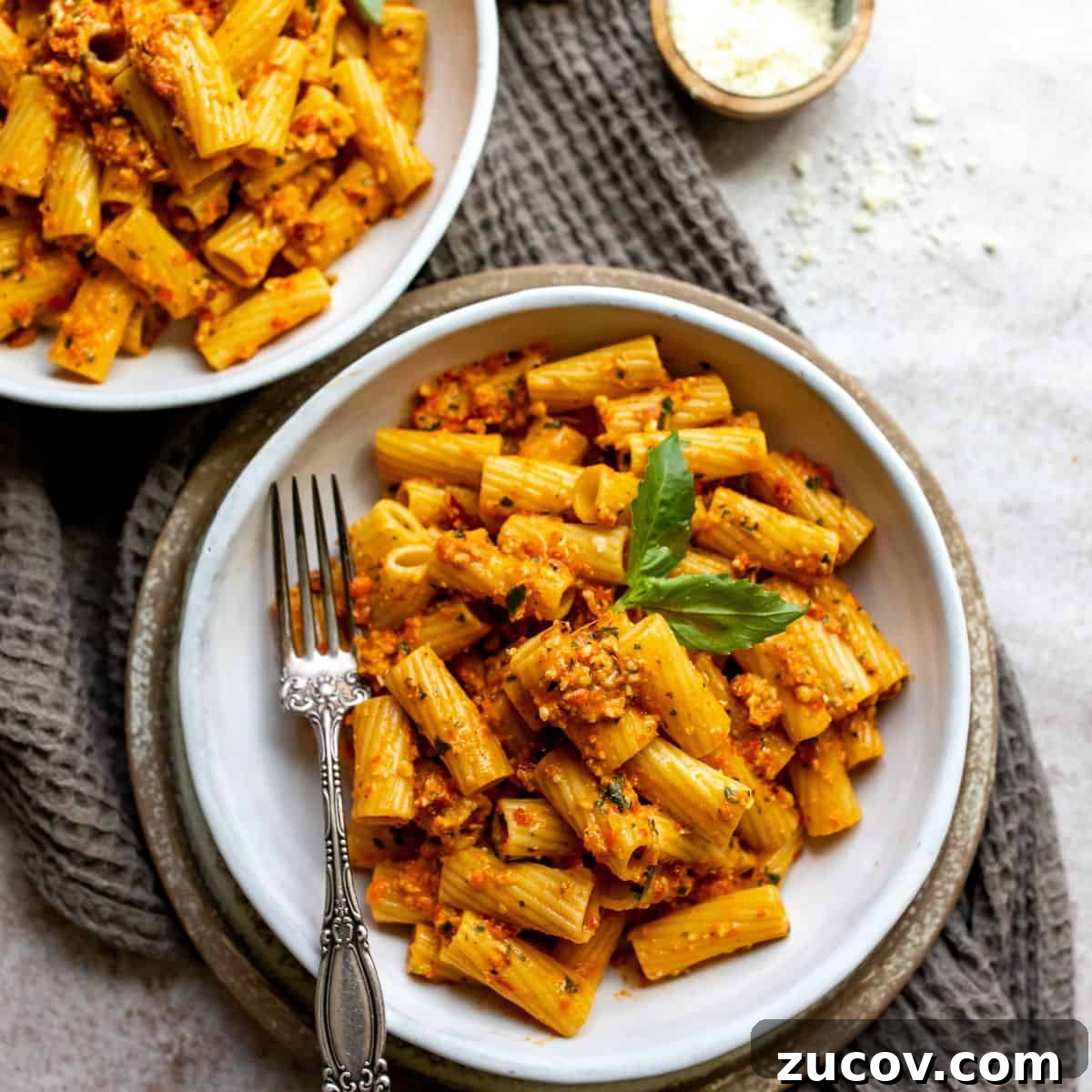 Roasted Red Pepper Pesto Recipe for Pasta, Sandwiches & Dips 6 Two white bowls with a silver fork ad red pesto and a sprig of basil.