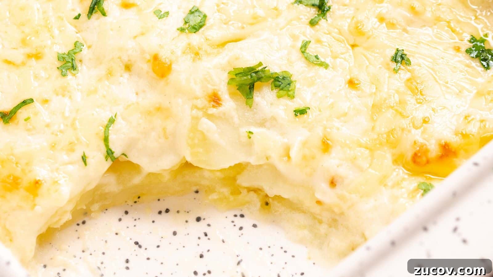 17 Comforting Side Dishes That Steal the Show 11 Close-up of a cheesy scalloped potatoes dish in a white baking dish, garnished with parsley.