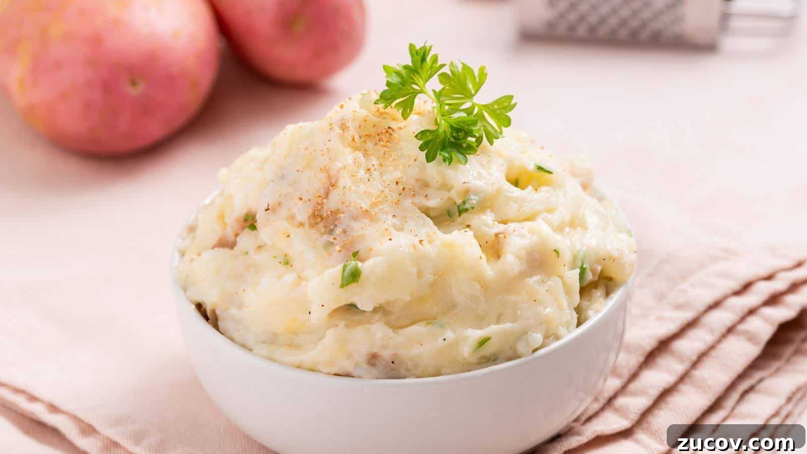 17 Comforting Side Dishes That Steal the Show 7 A bowl of mashed potatoes garnished with parsley, set on a pink cloth napkin, with whole potatoes and a grater in the background.