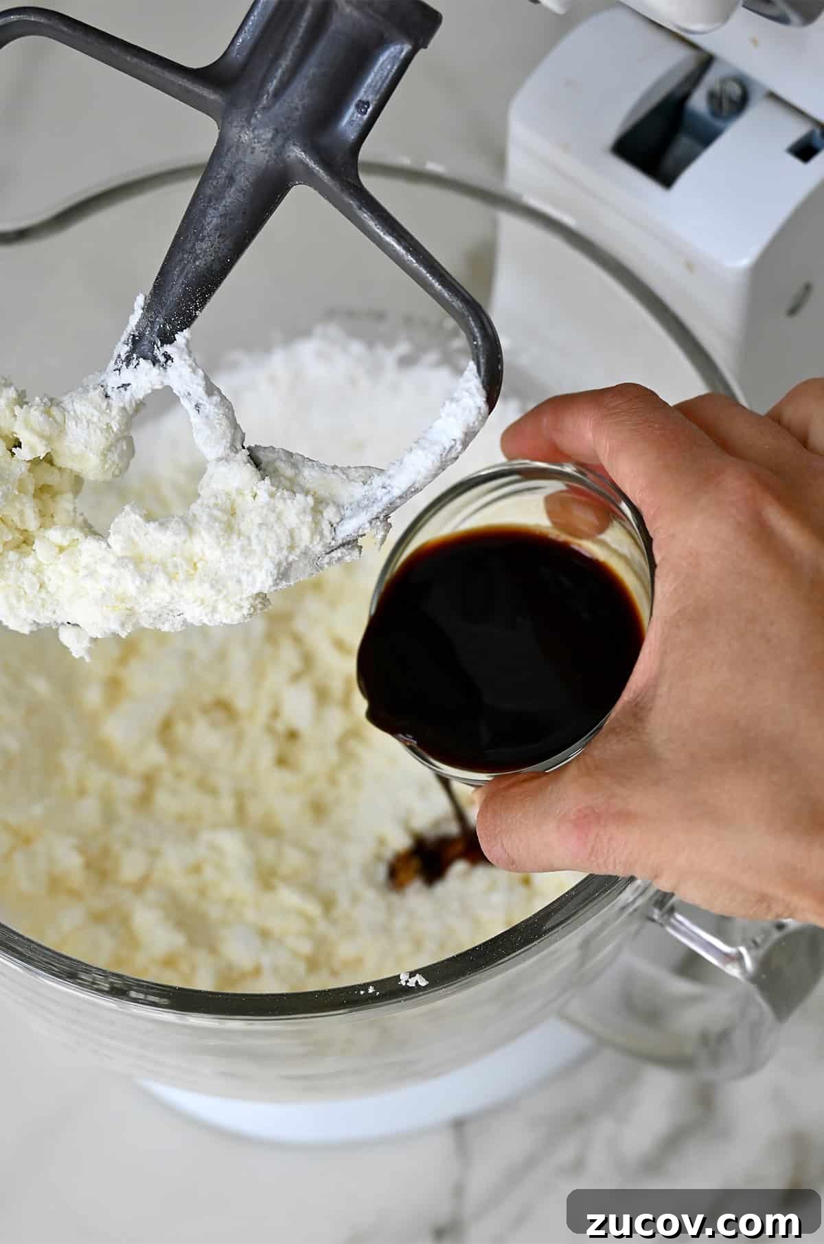 5-Minute Coffee Buttercream Frosting Recipe 7 Coffee from a small bowl being poured into the bowl of a stand mixer with buttercream frosting.