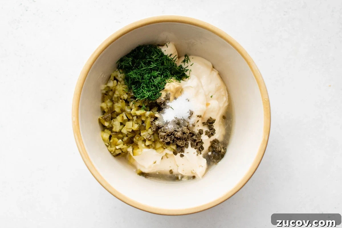Creamy Homemade Tartar Sauce Recipe for Fish and Seafood 4 Mixing bowl with mayonnaise, chopped dill pickles, minced dill, capers, Dijon mustard, sugar and lemon juice before mixing.