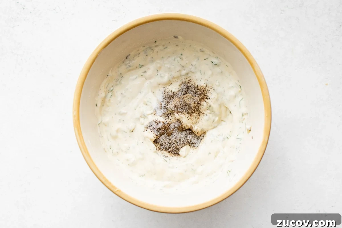 Creamy Homemade Tartar Sauce Recipe for Fish and Seafood 5 Partially mixed tartar sauce in a bowl with salt and pepper on top, ready to be stirred in.