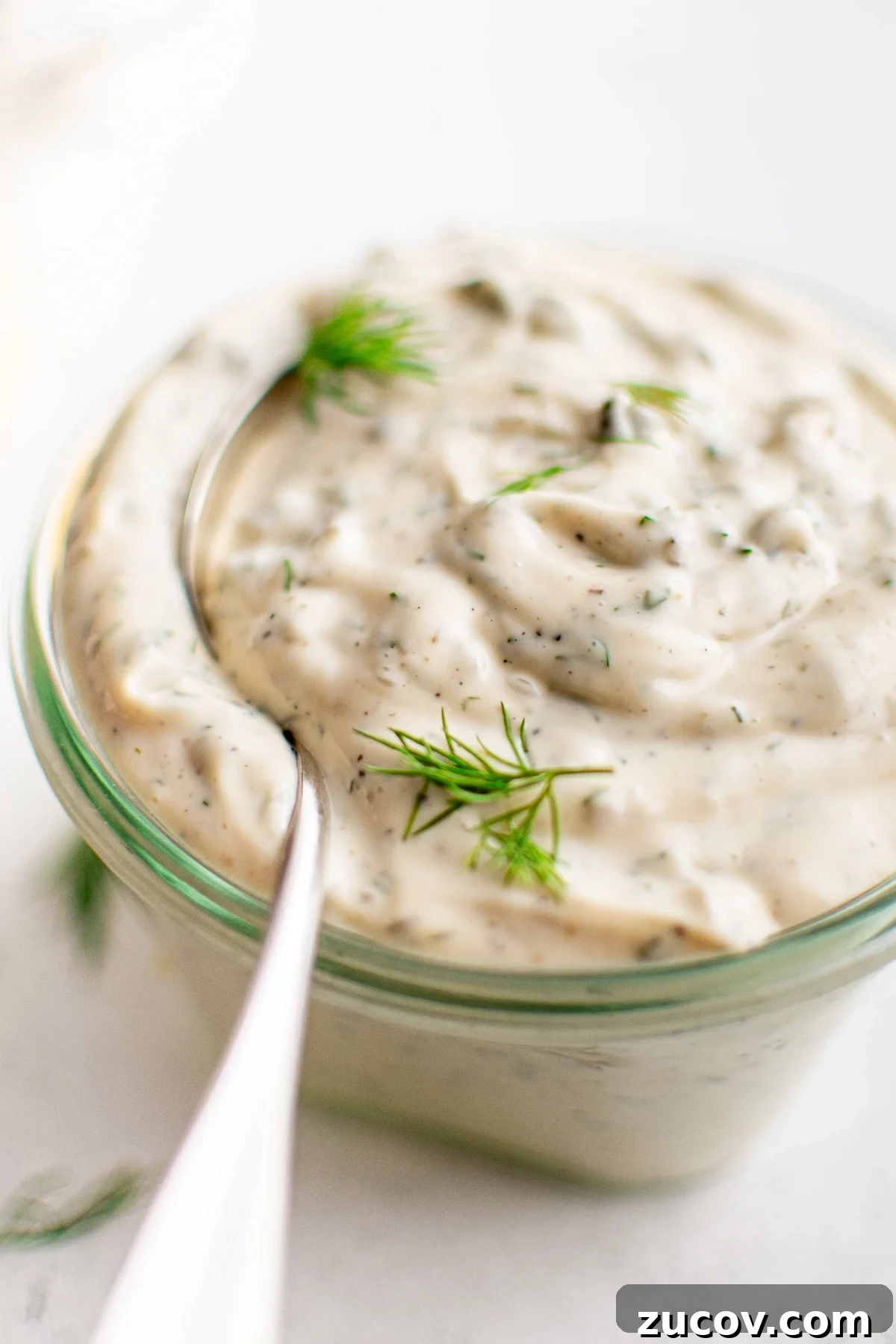 Creamy Homemade Tartar Sauce Recipe for Fish and Seafood 7 Close-up of tartar sauce in a small glass jar with a spoon dipped in, topped with fresh dill.