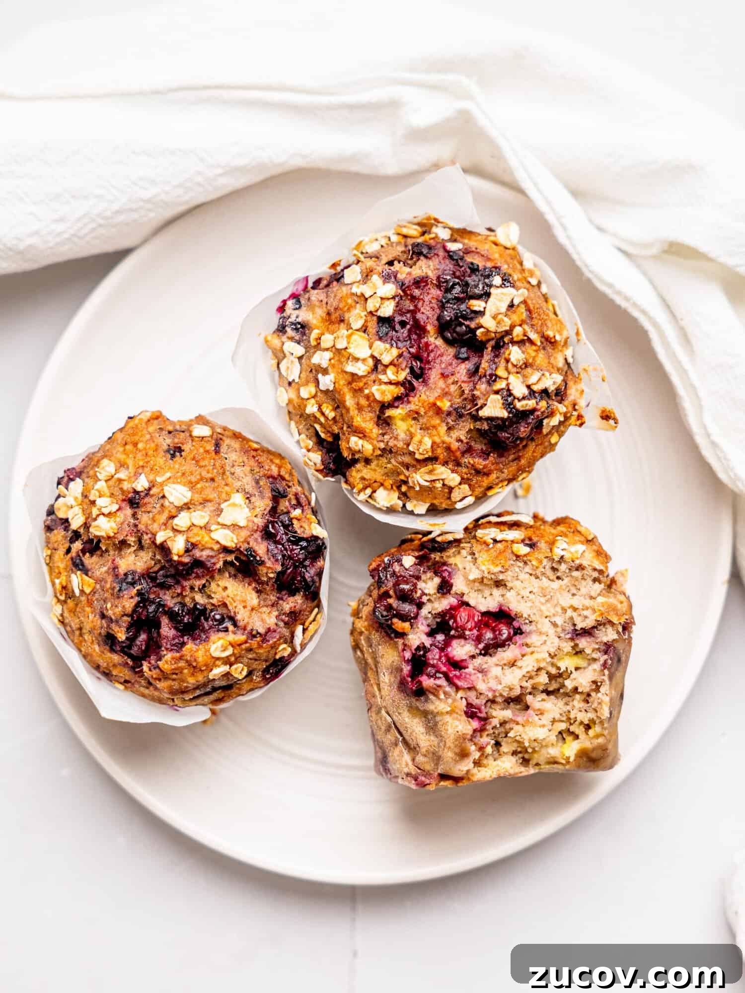 Banana Blackberry Muffins with 5 Simple Ingredients 7 Bird's eye view of three banana blackberry oatmeal muffins on a white plate.