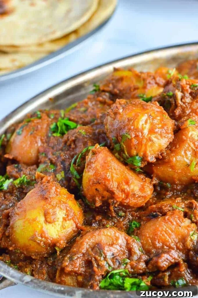 Bombay Potatoes Recipe: Restaurant-Style Spiced Potatoes 2 angled view of potatoes in brown sauce with fresh herbs sprinkled on top and roti in the background