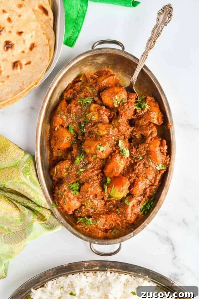 Bombay Potatoes Recipe: Restaurant-Style Spiced Potatoes 3 Top down view of a brown potato curry with chapati in the left corner and basmati rice at the bottom