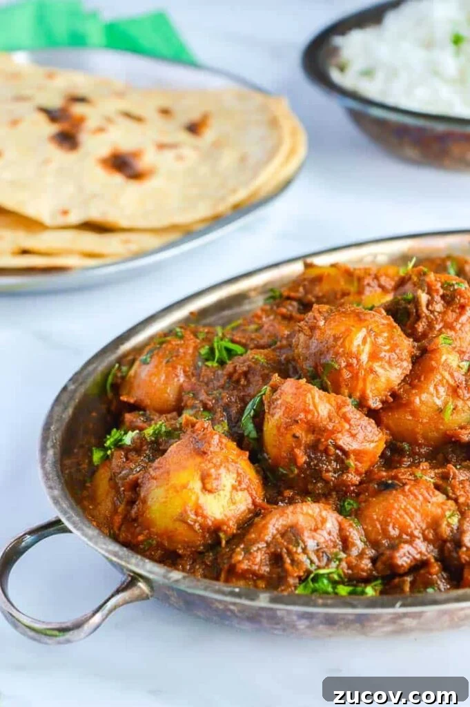 Bombay Potatoes Recipe: Restaurant-Style Spiced Potatoes 8 A silve pan of bombay potatoes with roti and rice in the background on a white surface