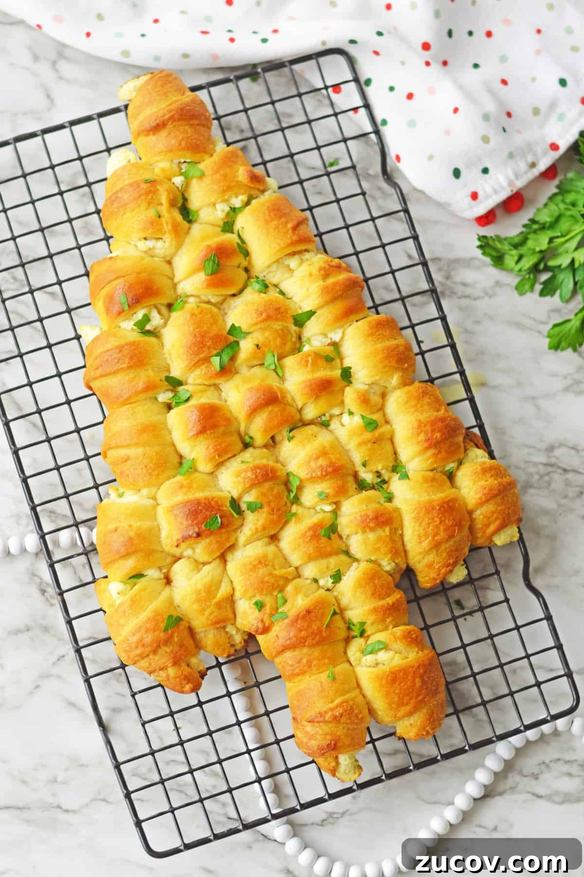 Pull-apart crescent roll Christmas Tree topped with melted butter and parsley on wire rack.